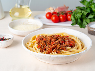 pasta bolognese with tomato sauce, ground minced beef, basil leaves on white table, linen napkin, side view