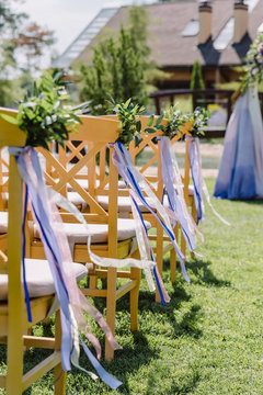 Wooden chairs at a wedding. The chairs decorated with buttonholes and tapes for guests