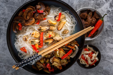 Traditional Asian food - rice noodles with seafood, salad, red pepper and fried mushrooms are on the side table. Close-up. Top view