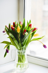 Floral background: bouquet of multicolored tulips in a glass vase on a light background, blank, mocap for mother's day greetings, international women's day