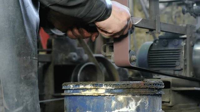 Grinding billets of metal knife on a belt-grinding machine. Close-up of a man's hands.