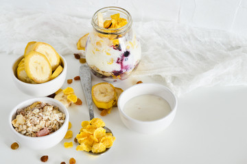 Breakfast in a jar: cornflakes, banana, fresh berries, granola, yogurt on a light background. The concept of healthy eating, high-carbon Breakfast.