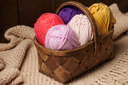 colorful wool yarn for knitting in basket, wooden background