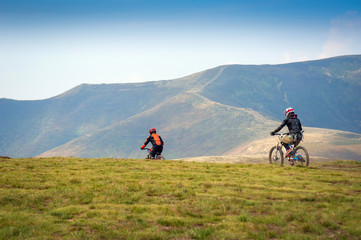 Obraz premium Professional cyclists riding the downhill mountain bike on the mountain trail. Two cyclists are preparing to ride mountain bike on single trail in Carpathians, Borzhava, Ukraine. 21 August, 2018.