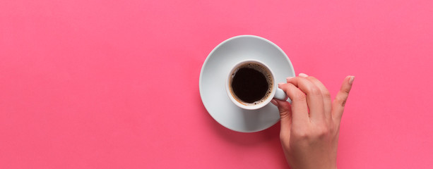 Minimalistic style woman hand holding a cup of coffee on pink background. Flat lay, top view banner