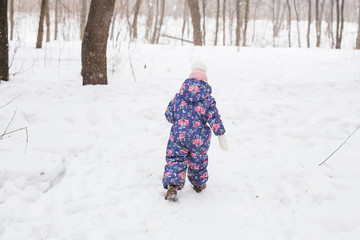 Fototapeta na wymiar Winter, childhood and nature concept - baby girl walking in the winter outdoors