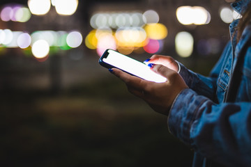 Woman pointing finger on blank screen smartphone on background bokeh light in night atmospheric city. hipster using in hands clean gadget mobile phone closeup, mockup street, online wifi internet