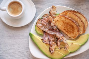 Fried bacon on white plate with cup of coffee and milk jug