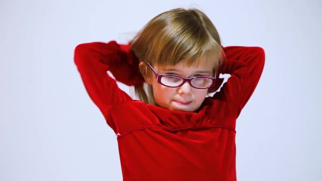 Nervous, shy little girl continually plays with hair while trying to think of what to say to the camera.  She is wearing a red dress and glasses.