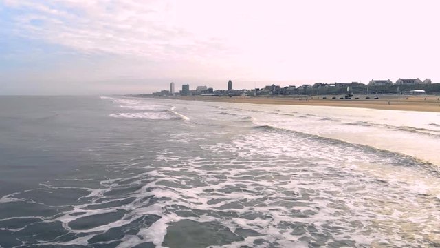 Aerial view. Slow motion flight over the sea and the waves that arrive to shore in the sunny morning. Netherlands Zandvoort. North Sea. Shore line