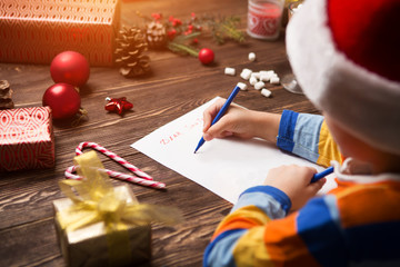 Child writes the letter to Santa Claus on wooden background with decorations.