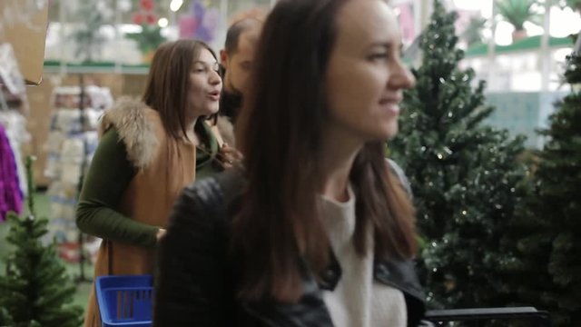 Group of friends at a Christmas sale at the supermarket, among the artificial Christmas trees to choose Christmas decorations.