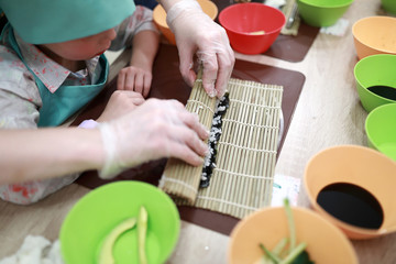 Kid rolling mat over sushi