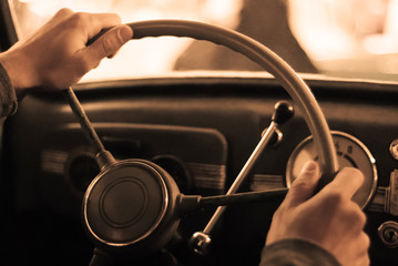 driving a vintage car; only the driver’s hand on the steering wheel are visible, the dashboard is blurred; stylized as an old sepia photo with dust and noise..