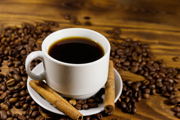 Cup of coffee, roasted coffee beans and cinnamon sticks on wooden table
