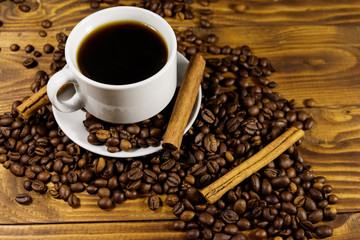 Cup of coffee, roasted coffee beans and cinnamon sticks on wooden table