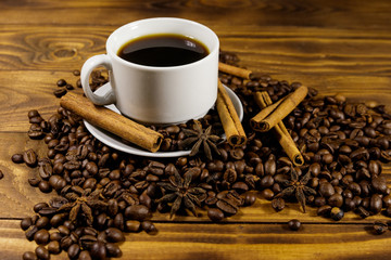 Cup of coffee, roasted coffee beans, star anise and cinnamon sticks on wooden table