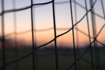 A closeup picture of a soccer net with a sunset sunrise in the background. detail ,sport, future, dreams, game football, goal, football goal;