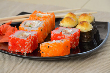 Sushi and rolls on a black plate with chopsticks.