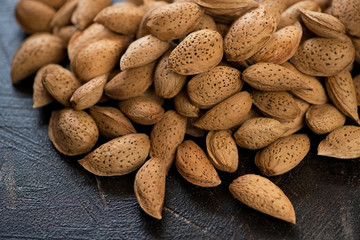 Close-up of unpeeled almonds over dark brown stone surface, horizontal shot