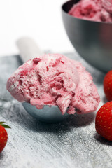 Strawberry ice cream scoop with chopped nuts and white chocolate on a rustic background