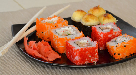 Sushi and rolls on a black plate with chopsticks.