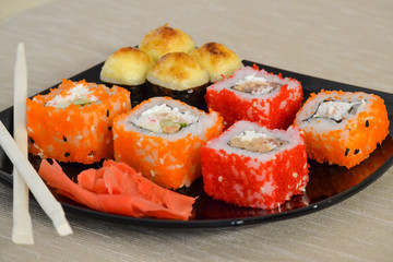 Sushi and rolls on a black plate with chopsticks.