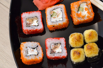 Sushi and rolls on a black plate with chopsticks. top view
