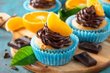 Orange Cupcakes with Chocolate Cream and Fresh Tangerines close-up on a blue stone or concrete...