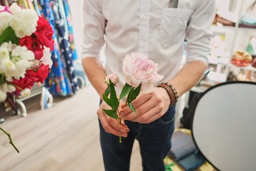 the guy in the white shirt holds a pink peony in his hand, focus on the flowers. on a beige background
