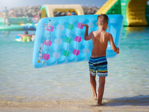 Cute European boy in striped swimming shorts is holding air mattress in his hands. He is running in to the sea and enjoying his holidays.