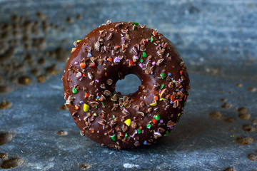 Tasty chocolate donut with frosting and candy sprinkle on grunge background