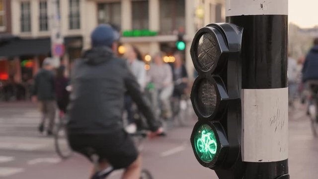 Many bicycles ride on Amsterdam street, in the foreground a special traffic light for cyclists. Environmentally friendly mode of transport
