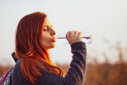 Young redhead girl drinks water 