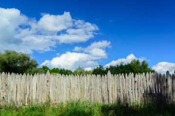 Fototapeta premium An old log fence and a blue sky with clouds. Security and fencing. Protection against thieves