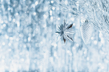 Shiny silver christmas ornaments hanging on a tree, with defocused christmas lights in the background.