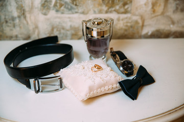 Men's accessories, leather belt, perfume, bow tie, groom's golden rings, watches and brides on a white table. Businessman clothing detail concept.