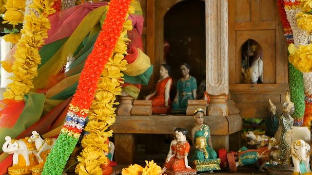 Wooden miniature guardian spirit house. Small buddhist temple shrine, colorful flower garlands. San phra phum erected to bring fortune. Traditional respect animistic rituals, pray ceremonies