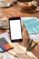 Womans hand holds modern cell phone with blank screen, watches video online, messages with followers, poses in coworking space, connected to high speed internet. Copy space area for website.