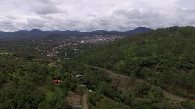 Aerial drone shot of a mountain town surrounded by lush trees in Mexico