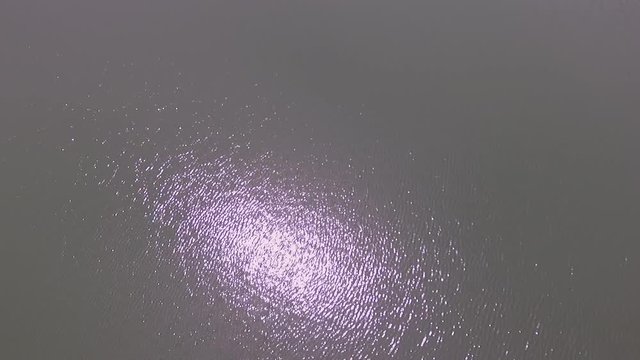Aerial drone shot of sun reflecting in a crater lake and the water rippling