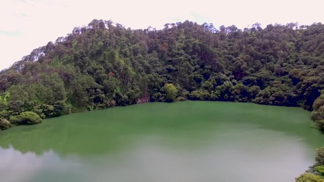 Drone aerial shot flying over a volcanic crater lake surrounded by trees