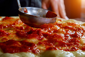 Chef hand putting classical tomato sauce on pizza base