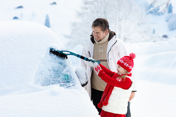 Father and child brushing off car in winter.
