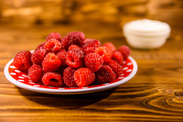Ceramic plate with ripe raspberries and sour cream on wooden table