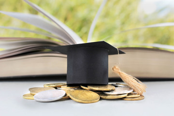 Graduation Cap for savings coins for scholarships for funding and education. Graduation microcline and gold coins and book on a green background, the concept of investment education, closure,