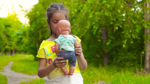 Girl feeding and kissing baby doll in park