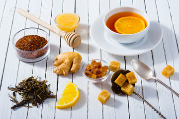 cup of tea, different leaves, honey, lemon ginger and brown sugar on white wooden table background