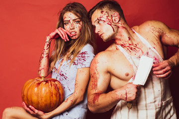 Creepy scary halloween vampire girl and big muscular man looking camera and holding pumpkin. Halloween girl with a carved Pumpkin. Isolated on red background.