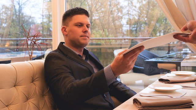 Handsome guy (man) in a suit restaurant, gets a menu. Concept of: Menu, Orders, Waiter, Business, Beautiful atmosphere, Lifestyle.